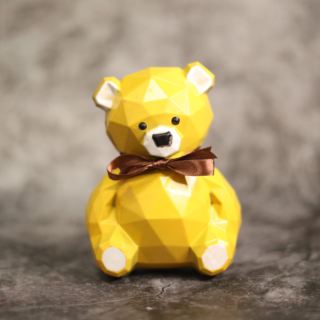 Yellow teddy bear figurine with a brown bow tie on a gray background